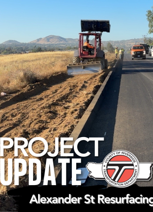 Construction workers and machinery resurfacing Alexander Street alongside a rural road with mountains in the background.